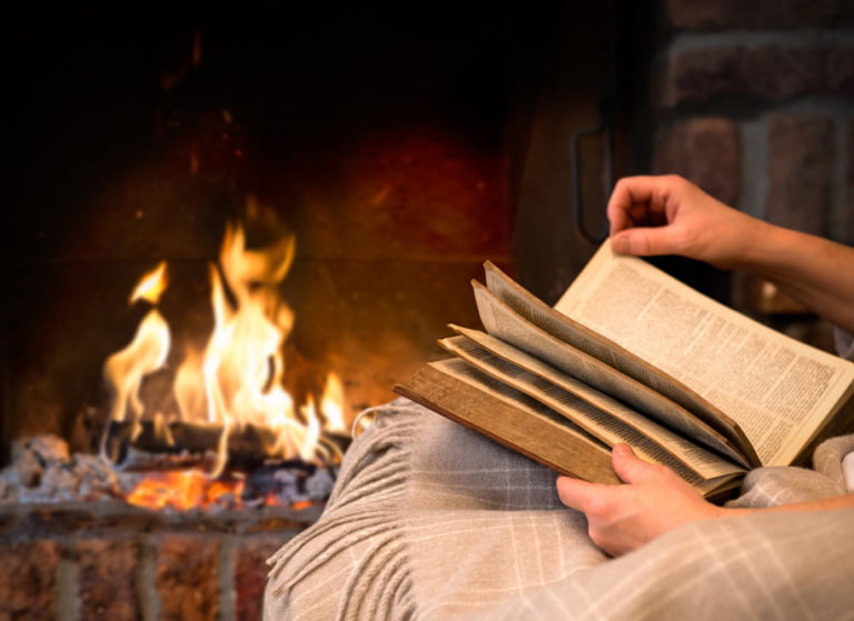Person reading a crime novel by a fireplace.