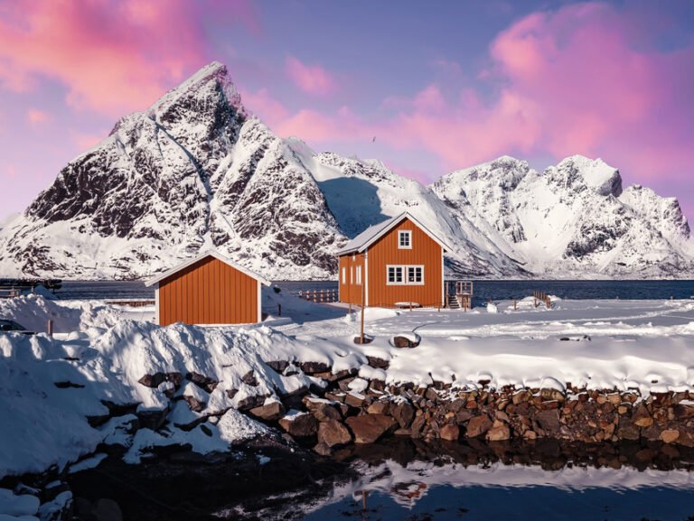 Yellow cabins against the white snowy mountains and pink sky in Lofoten.